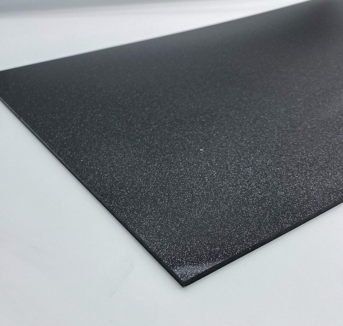 Black glitter acrylic sheet corner close-up, dark sparkling texture on edge