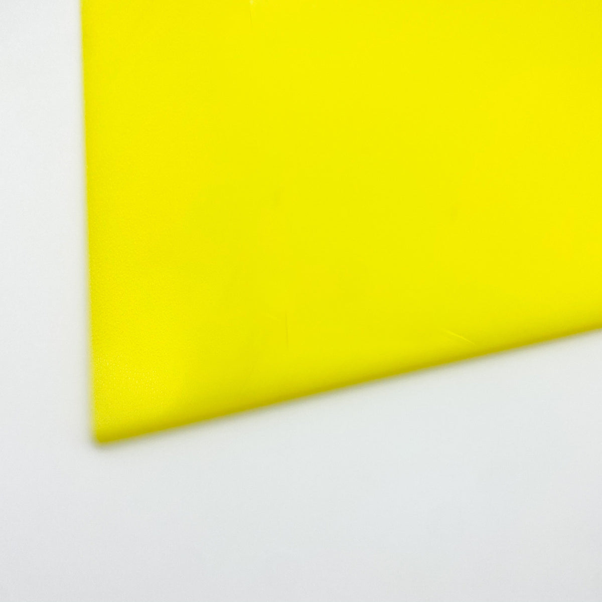 Fluorescent neon yellow cast acrylic sheet close-up, smooth glossy finish